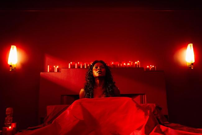 Bilquis im Bett in einem Zimmer mit roter Beleuchtung