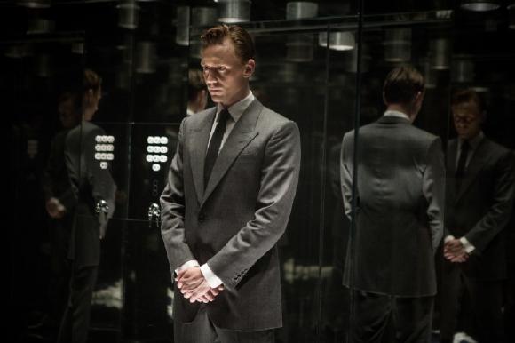 Tom Hiddleston in Anzug und zurückgekämmten Haaren in einem verspiegelten Aufzug